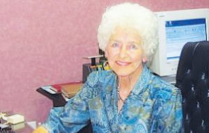 Treasure: a woman in a blue dress sitting at a desk smiling at the camera